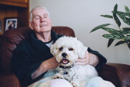 Älterer Mann hat einen kleinen weißen Hund auf dem Schoß, Foto: iStock DGLimages