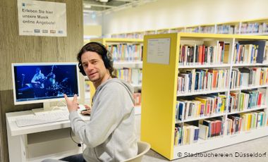 Foto von Audio- und Video-Rechner in der Musikbibliothek. Davor sitzt ein junger Mann mit Kopfhörern.