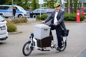 Foto von Manfred Golschinski, Leiter des Amtes für Statistik und Wahlen, der eins der Lastenräder testet und vorne im Korb des Lastenrades eine Wahlurne transportiert.