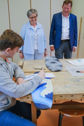 Stadtdirektor Burkhard Hintzsche und Dagmar Wandt, Leiterin des Amtes für Schule und Bildung, lassen sich von einem Teilnehmer der Adventure School erklären, wie die Longboards entstehen