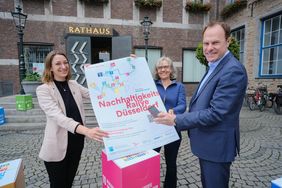 Oberbürgermeister Dr. Stephan Keller eröffnet die Nachhaltigkeits-Rallye am Rathaus. Philomena Lamberty (l.) und Ursula Keller (M.) (Geschäftsstelle Nachhaltigkeit) präsentieren eines der Plakate zur Rallye. Foto: Gstettenbauer.