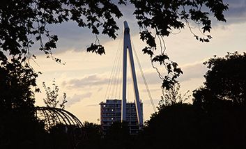 Eine Fußgängerbrücke am Abend von der Île du Ramier über die Garonne in Toulouse mit dem Stadtpanorama im Hintergrund.