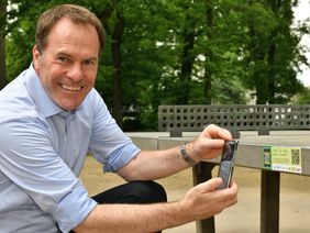 Oberbürgermeister Dr. Stephan Keller scannt an der Steinplatte im Hofgarten mit dem Handy den QR-Code zur Breitensport-Kampagne "Düsseldorf spielt Tischtennis. Für Düsseldorf."; Foto: MaJo-Foto