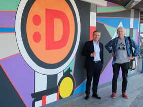 Oberbürgermeister Thomas Geisel (links) und Künstler Klaus Klinger von Farbfieber e.V. vor dessen Kunstwerk am S-Bahnhof Wehrhahn. Foto: Wilfried Meyer