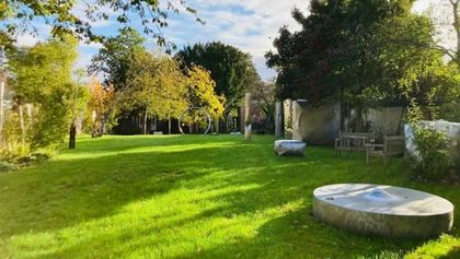 Der weitläufige, grüner Skulpturengarten des Künstlerhaus Werthmann-Heyne mit gepflegtem Rasen, dichten Bäumen und modernen Steinskulpturen im warmen Sonnenlicht