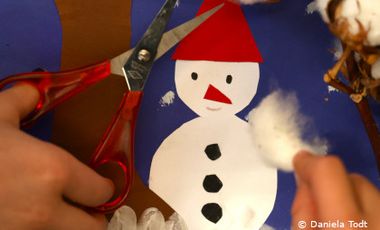 Foto von Kinderhänden, die mit Schere, Papier und Watte einen Schneemann basteln.