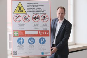 Oberbürgermeister Dr. Stephan Keller mit einem neuen Schild, das eindringlich auf die Lebensgefahr hinweist, die beim Baden im Rhein droht. Foto: Michael Gstettenbauer