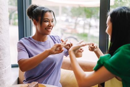 Zwei junge Frauen bei Gebärdensprache beim Plaudern im Café, Foto: iStock, Mariia Vitkovska