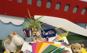 Foto aus dem Kinderbereich in der Bücherei Unterrath mit einem Holzflugseug an der Wand, Kuscheltieren und Bastelsachen im Vordergrund.
