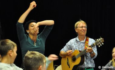 Zwei Personen, ein Mann spielt Gitarre und neben ihm tanzt eine Frau gestikulierend dazu